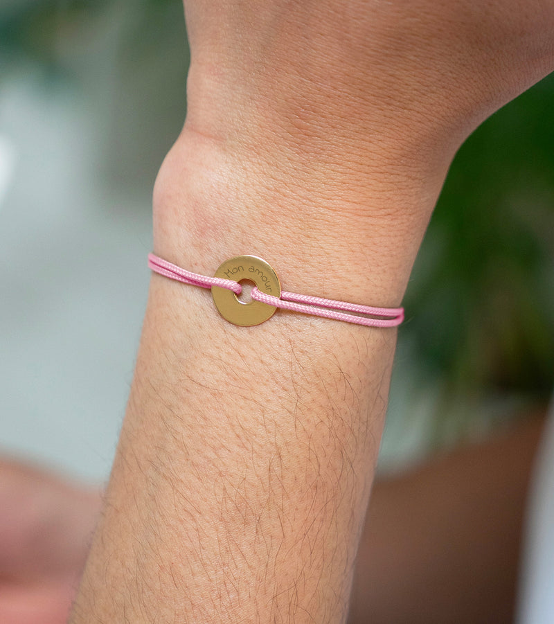 Le bracelet en plaqué or adopte une forme cible personnalisée en 15mm, accompagnée d'un cordon rose.