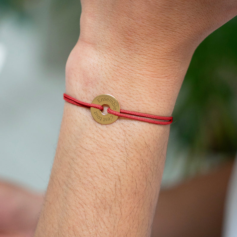 Un bracelet forme cible, personnalisé en 15mm, plaqué or, avec un cordon rouge.