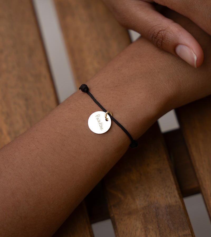 Un bracelet en plaqué or avec une médaille de 15mm, monté sur un cordon noir élégant.