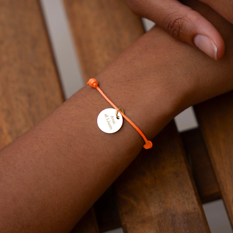 Exprimez votre personnalité avec ce bracelet élégant, composé d'une médaille plaquée or de 15mm sur un cordon orange fluo.