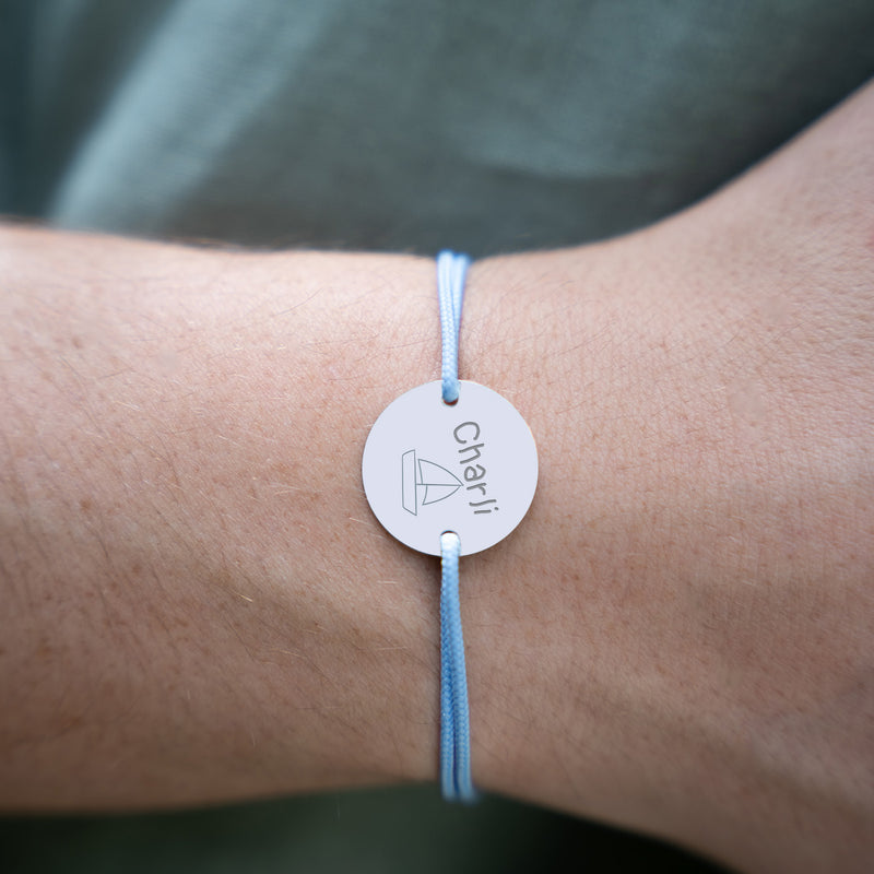 Un bracelet en argent, paré d'une médaille personnalisée de 15mm à deux trous, se démarque sur un cordon bleu pastel