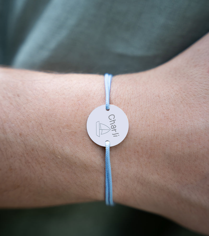 Un bracelet en argent, paré d'une médaille personnalisée de 15mm à deux trous, se démarque sur un cordon bleu pastel