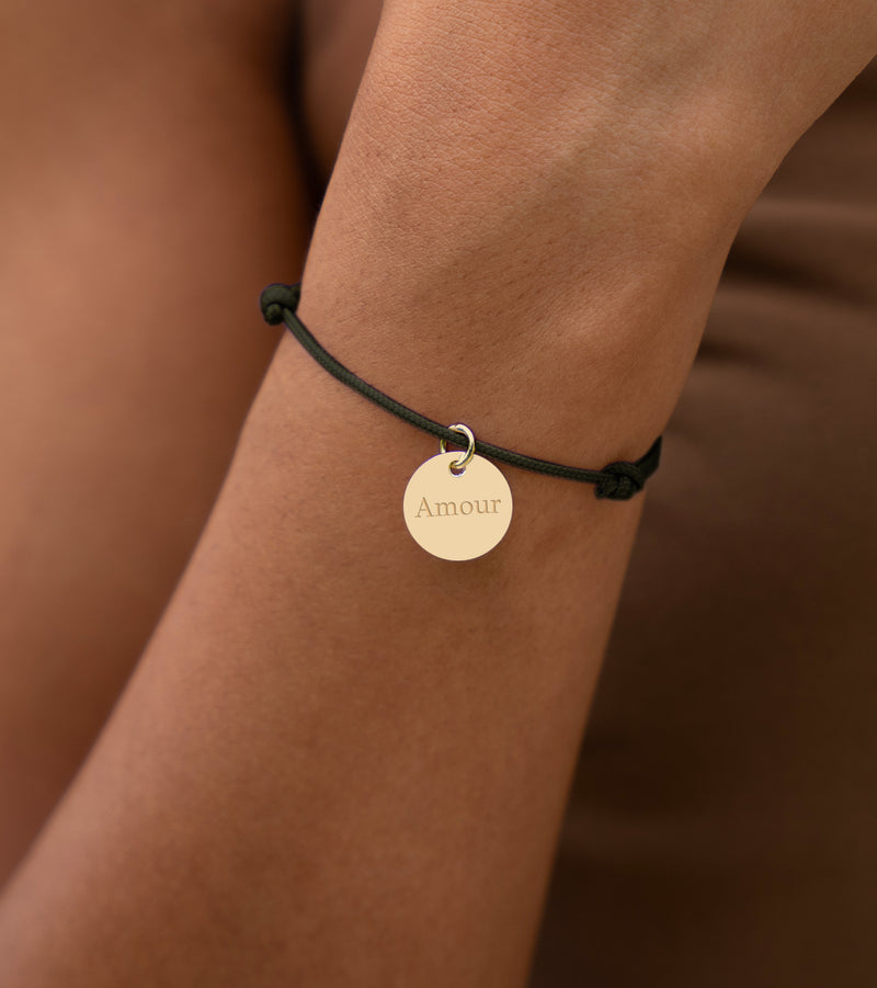Un bracelet orné d'une médaille dorée de 15mm sur un cordon de couleur kaki.