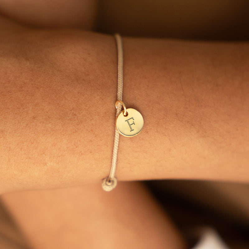 Bracelet en plaqué or 10mm avec médaille personnalisée sur cordon beige, un accessoire élégant pour votre style.