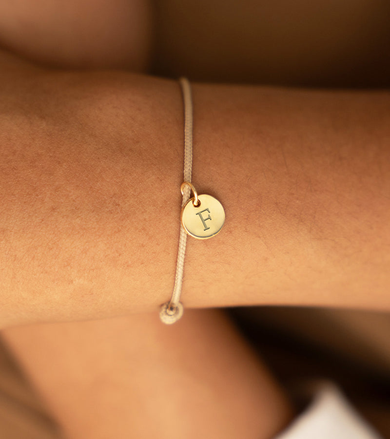 Bracelet en plaqué or 10mm avec médaille personnalisée sur cordon beige, un accessoire élégant pour votre style.
