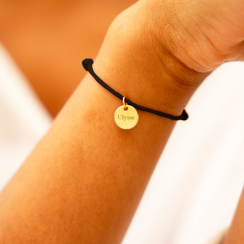 Accessoire de mode haut de gamme, un bracelet plaqué or avec médaille de 10mm, rehaussé par un cordon noir tendance.
