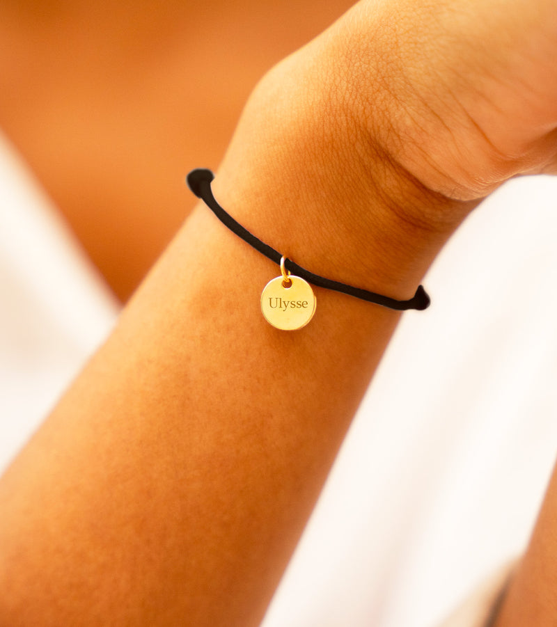 Accessoire de mode haut de gamme, un bracelet plaqué or avec médaille de 10mm, rehaussé par un cordon noir tendance.