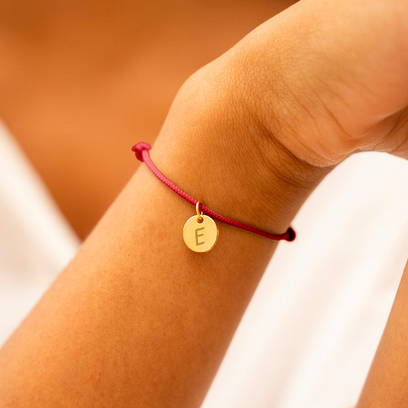 Une médaille plaquée or de 10mm sur un bracelet en cordon rouge, parfait pour afficher votre style avec sophistication.