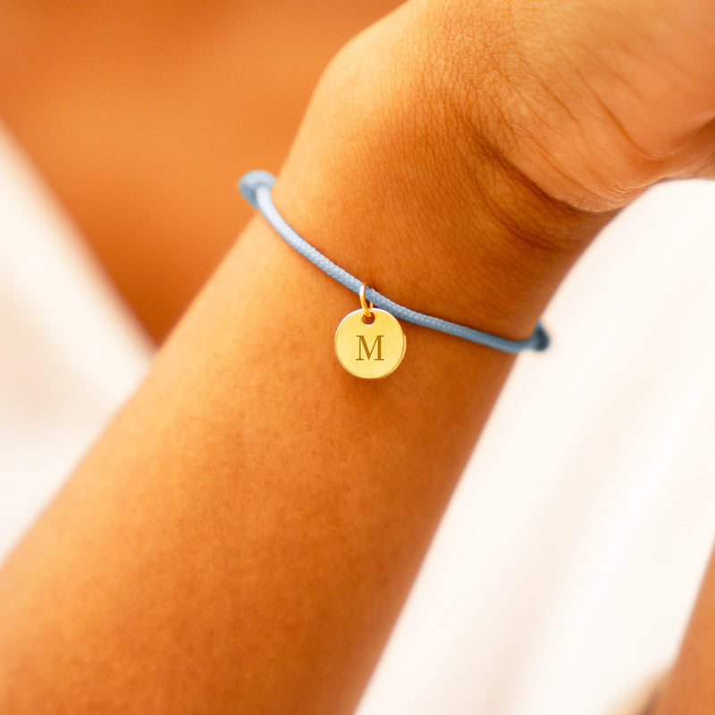 Un bracelet élégant en plaqué or, avec une médaille de 10mm, monté sur un cordon bleu pastel.