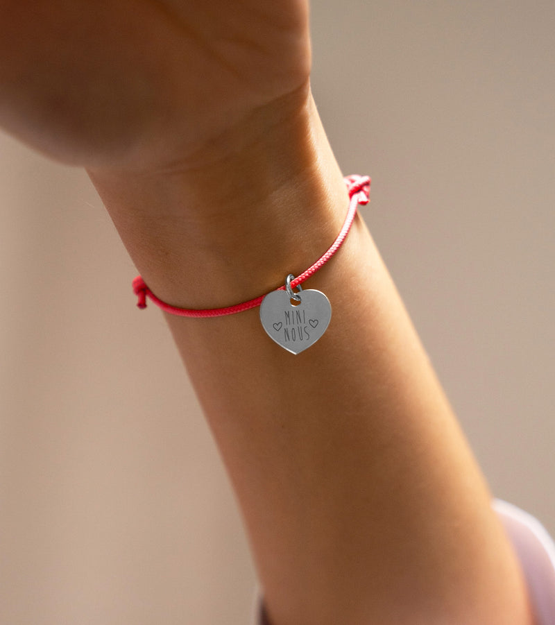 Voici un bracelet en argent orné d'un cœur, accompagné d'un cordon rose fuchsia.