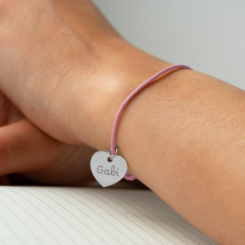 Un bracelet délicat avec un cœur argenté de 15mm de taille, attaché à un cordon rose.