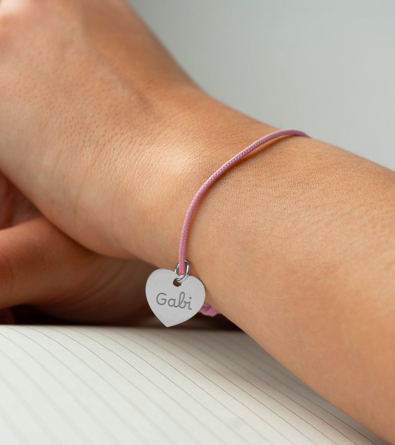 Un bracelet délicat avec un cœur argenté de 15mm de taille, attaché à un cordon rose.