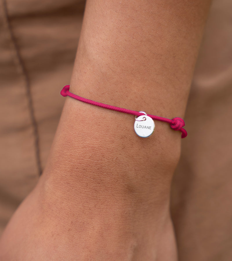Médaille argentée de 10mm montée sur un bracelet en cordon rose fuchsia, un accessoire chic.