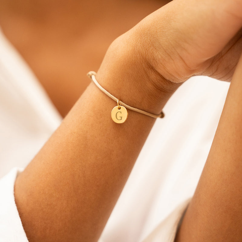 Bracelet cordon beige avec médaille plaquée or 10mm, un accessoire chic pour votre look quotidien.