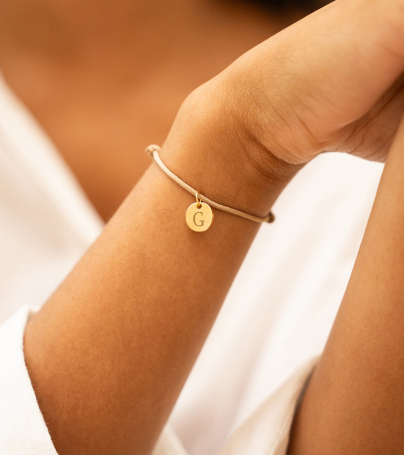 Bracelet cordon beige avec médaille plaquée or 10mm, un accessoire chic pour votre look quotidien.