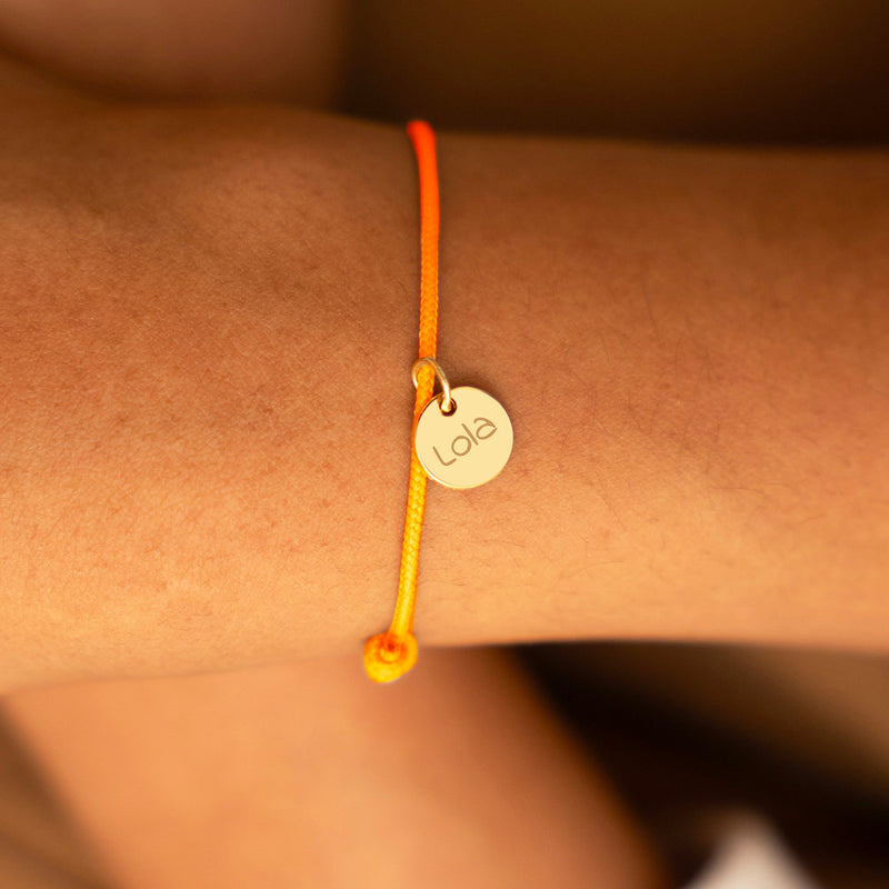 Bracelet avec une médaille dorée de 10 mm et un cordon orange fluorescent.