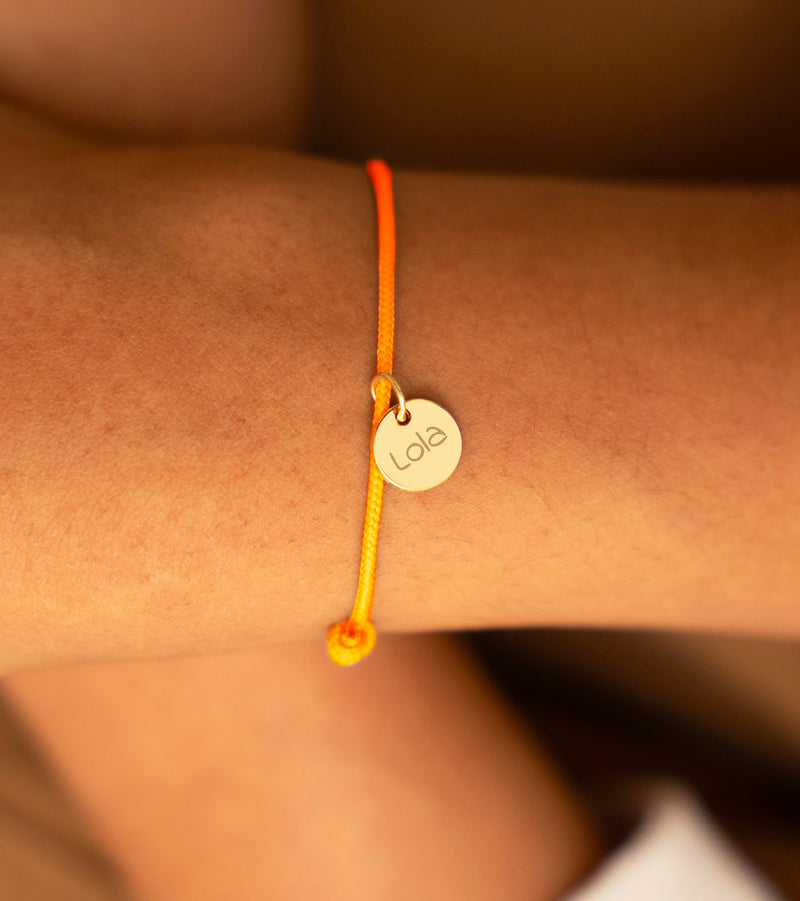 Bracelet avec une médaille dorée de 10 mm et un cordon orange fluorescent.