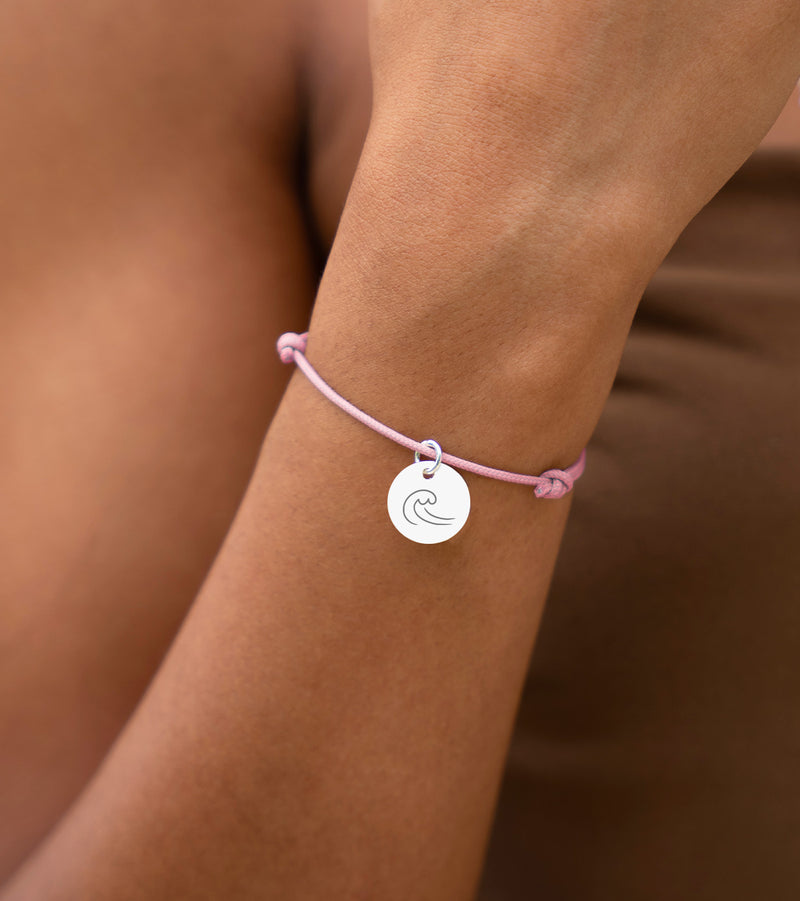 Un bracelet argenté avec une médaille de 15mm sur un cordon rose.