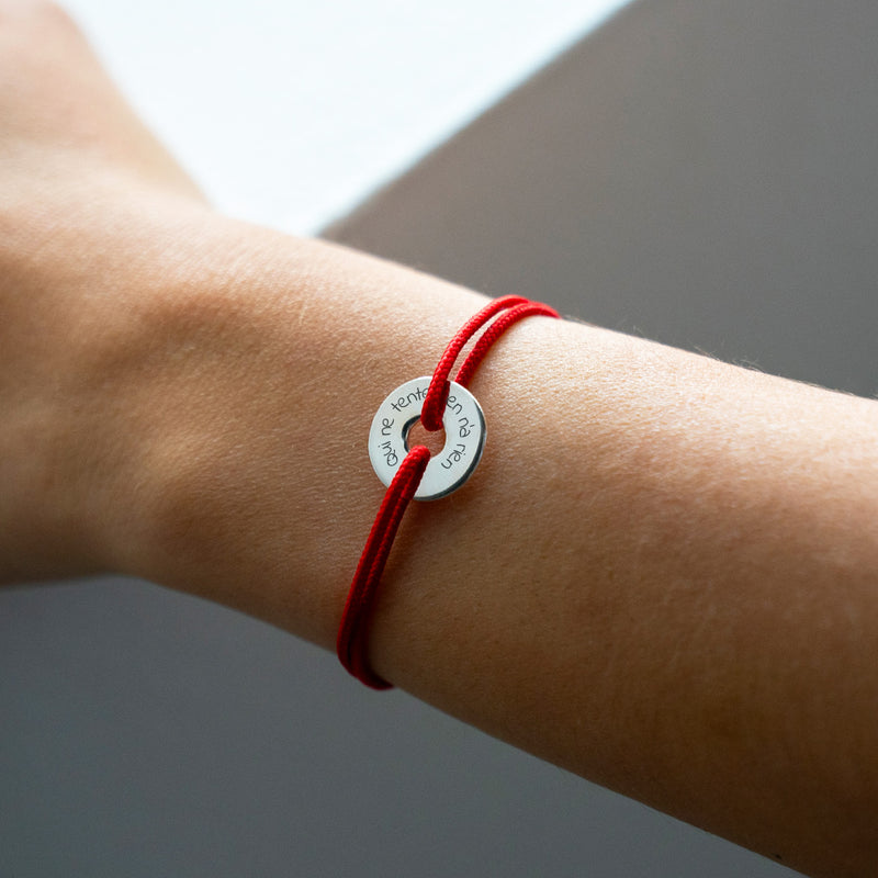 Arborant un cordon rouge, ce bracelet en forme de cible est personnalisé de 15mm en argent.