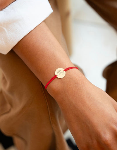 Ce bracelet, avec sa médaille plaquée or de 15mm, fixée par deux trous, s'orne d'un cordon rouge.