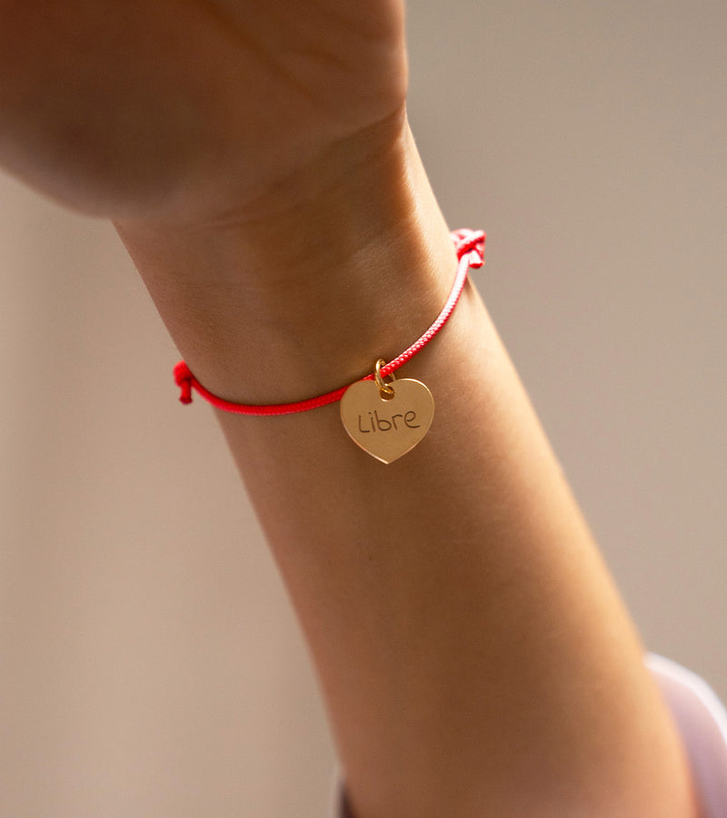 Sur fond orange fluo, un bracelet cœur personnalisé de 15mm en plaqué or brille avec élégance, souligné par un cordon vif.