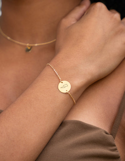 Bracelet en plaqué or, agrémenté d'une médaille personnalisée de 15mm, offre une touche de raffinement avec sa chaîne plate et ses deux trous distinctifs.