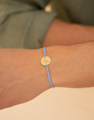 Ce bracelet, orné d'une médaille de 15mm et de deux trous, est plaqué or avec un cordon bleu pastel.