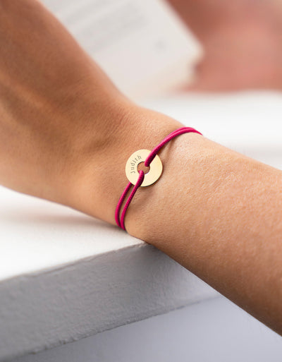 Un bracelet forme cible, personnalisé en 15mm, plaqué or, avec un cordon rose fuchsia.