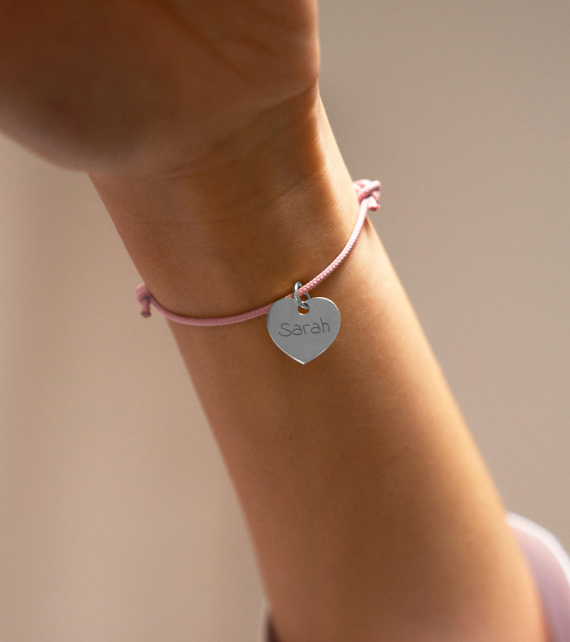 Ce bracelet argenté en forme de cœur mesure 15mm de diamètre, accroché à un cordon rose.