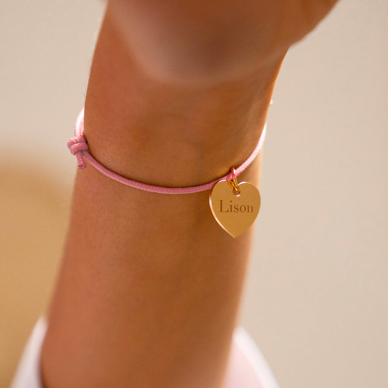 Bracelet en forme de cœur, plaqué or, sur un cordon rose.