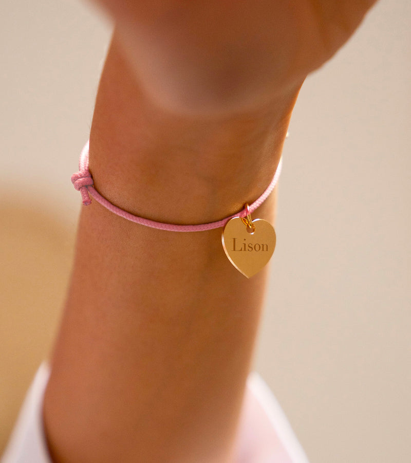 Bracelet en forme de cœur, plaqué or, sur un cordon rose.
