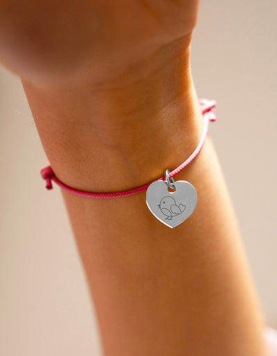 Découvrez ce bracelet argenté avec un cœur et un cordon rose fuchsia.