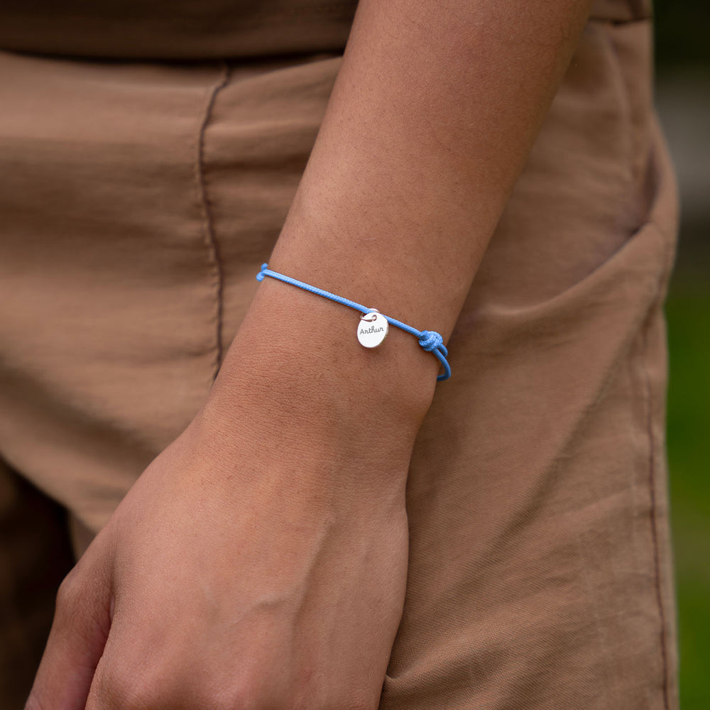 Une photo montrant un bracelet personnalisé avec une médaille en argent de 10mm sur un cordon de couleur bleu pastel.