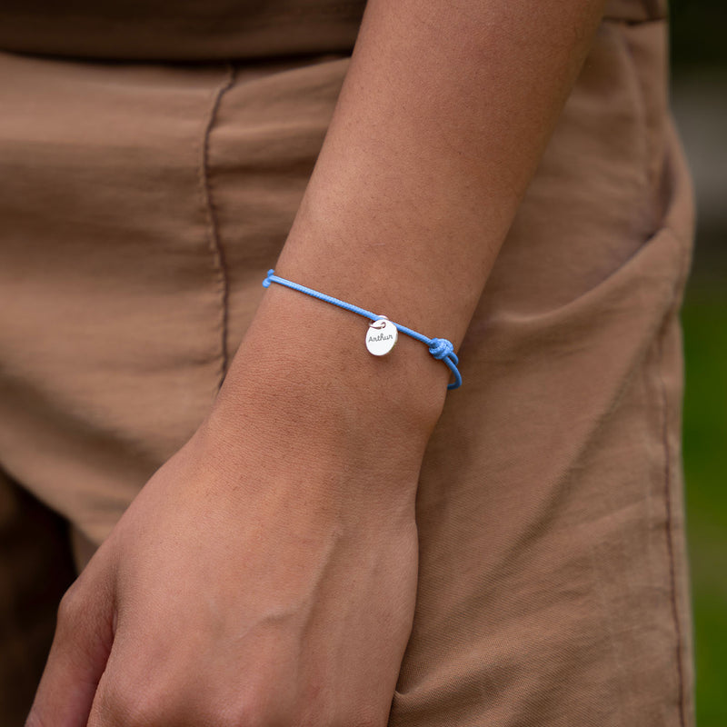 Une photo montrant un bracelet personnalisé avec une médaille en argent de 10mm sur un cordon de couleur bleu pastel.