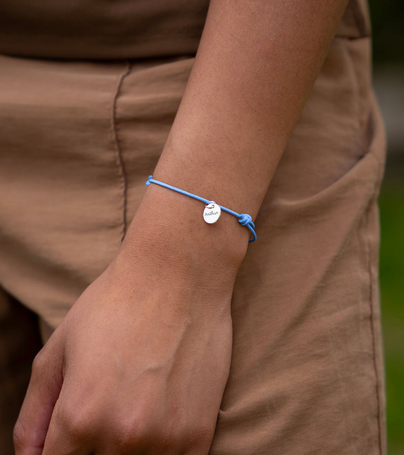 Une photo montrant un bracelet personnalisé avec une médaille en argent de 10mm sur un cordon de couleur bleu pastel.