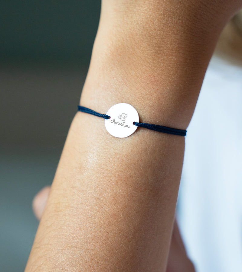 Médaille argentée de 15mm, suspendue à un bracelet, rehaussée d'un cordon bleu marine.