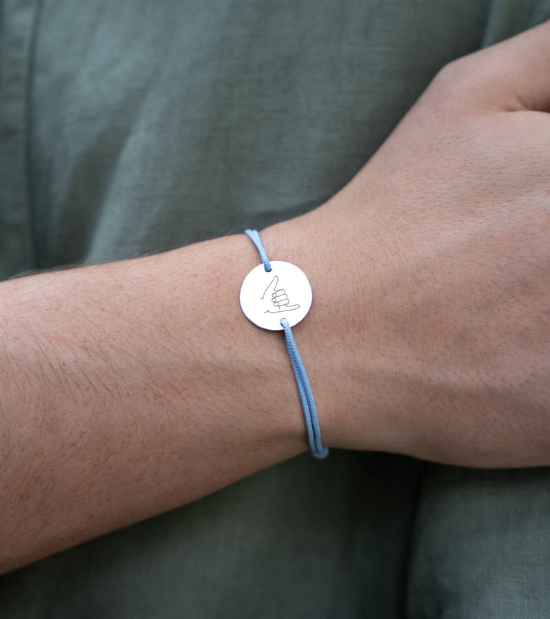 Sur fond de cordon bleu pastel, un bracelet en argent accueille une médaille de 15mm personnalisée avec deux trous.