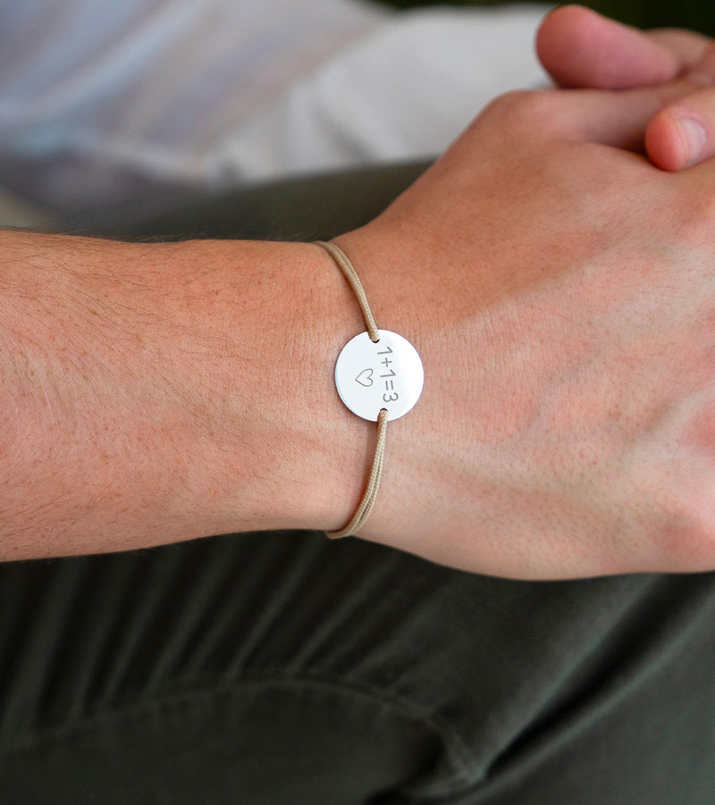 Un bracelet argenté avec une médaille de 15mm à personnaliser, complété par deux trous pour un cordon beige.
