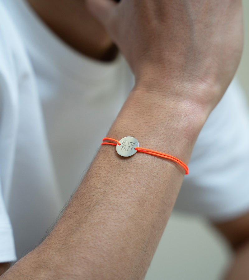 "Une médaille de 15mm personnalisée, encerclée par un cordon orange fluo, sur un bracelet argenté à deux trous. "