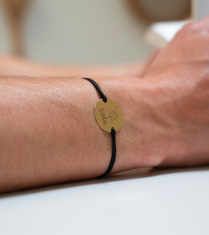 Un bracelet personnalisé avec une médaille en 20mm, deux trous en plaqué or, et un cordon noir pour une touche d'élégance.