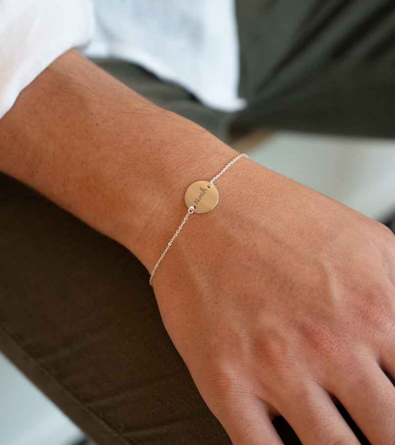 Une médaille personnalisée de 15mm suspendue à un bracelet en argent, deux trous assurent sa fixation. La chaîne plate offre une élégance discrète à ce bijou unique.