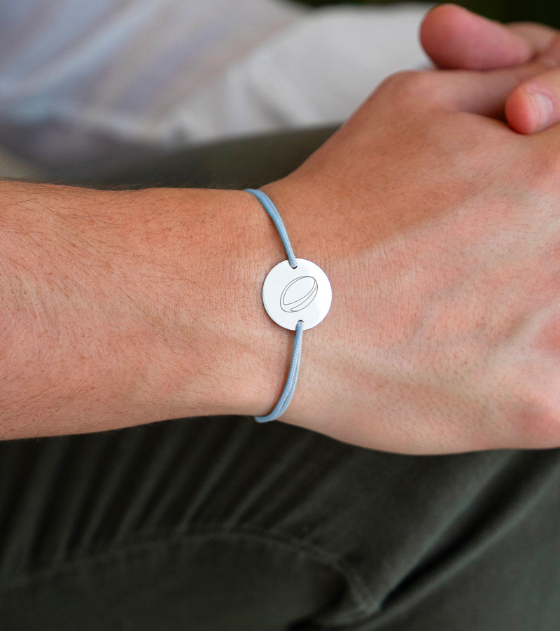 Une délicate médaille personnalisée de 15mm, montée sur un bracelet argenté à deux trous, contraste avec élégance le cordon bleu pastel
