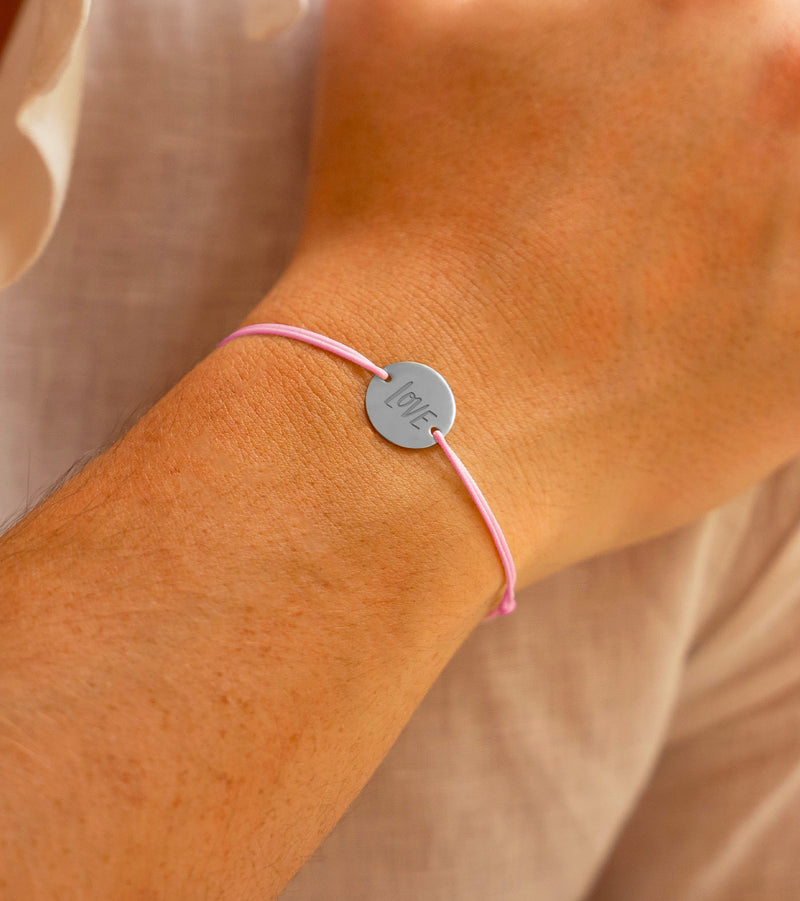 Un bracelet argenté lumineux, orné d'une médaille de 15mm personnalisée munie de 2 trous, associé à un cordon rose charmant