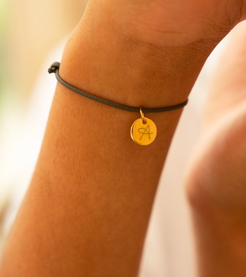 Un bracelet en cordon kaki avec une médaille plaquée or de 10mm, personnalisable à votre nom.