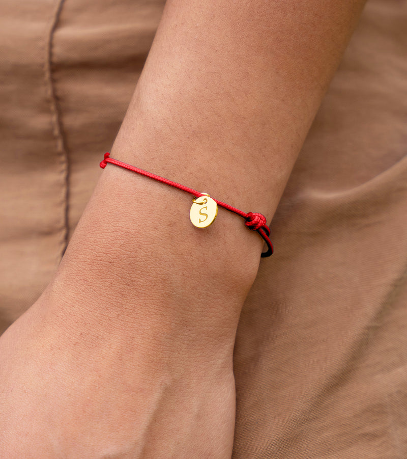 Un bracelet en cordon rouge orné d'une médaille plaquée or de 10mm, un accessoire chic pour votre poignet.