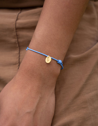 Un magnifique bracelet en plaqué or avec une médaille de 10mm, attaché à un cordon bleu pastel.