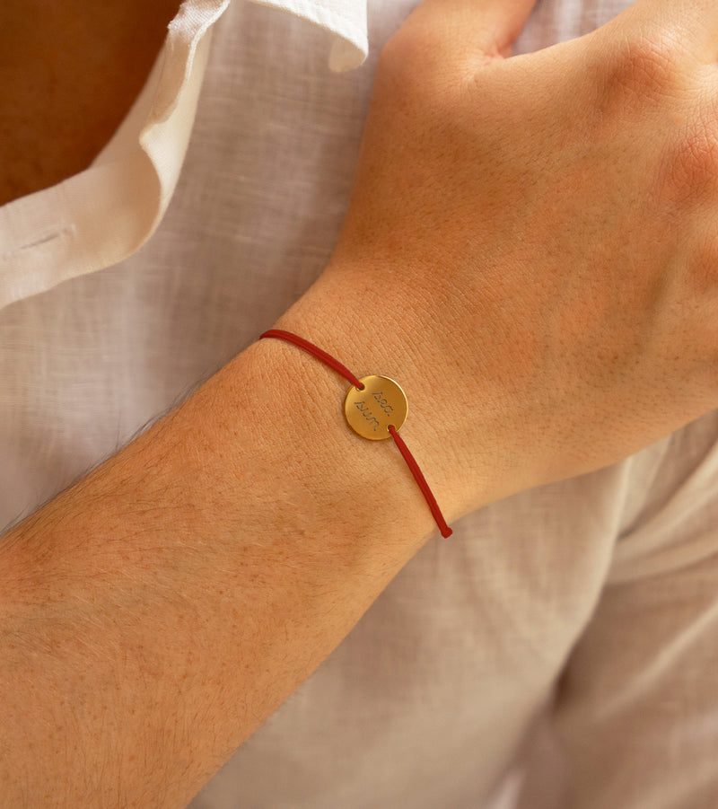  médaille plaquée or de 15mm, maintenue par deux trous, ce bracelet personnalisé se pare d'un cordon rouge.