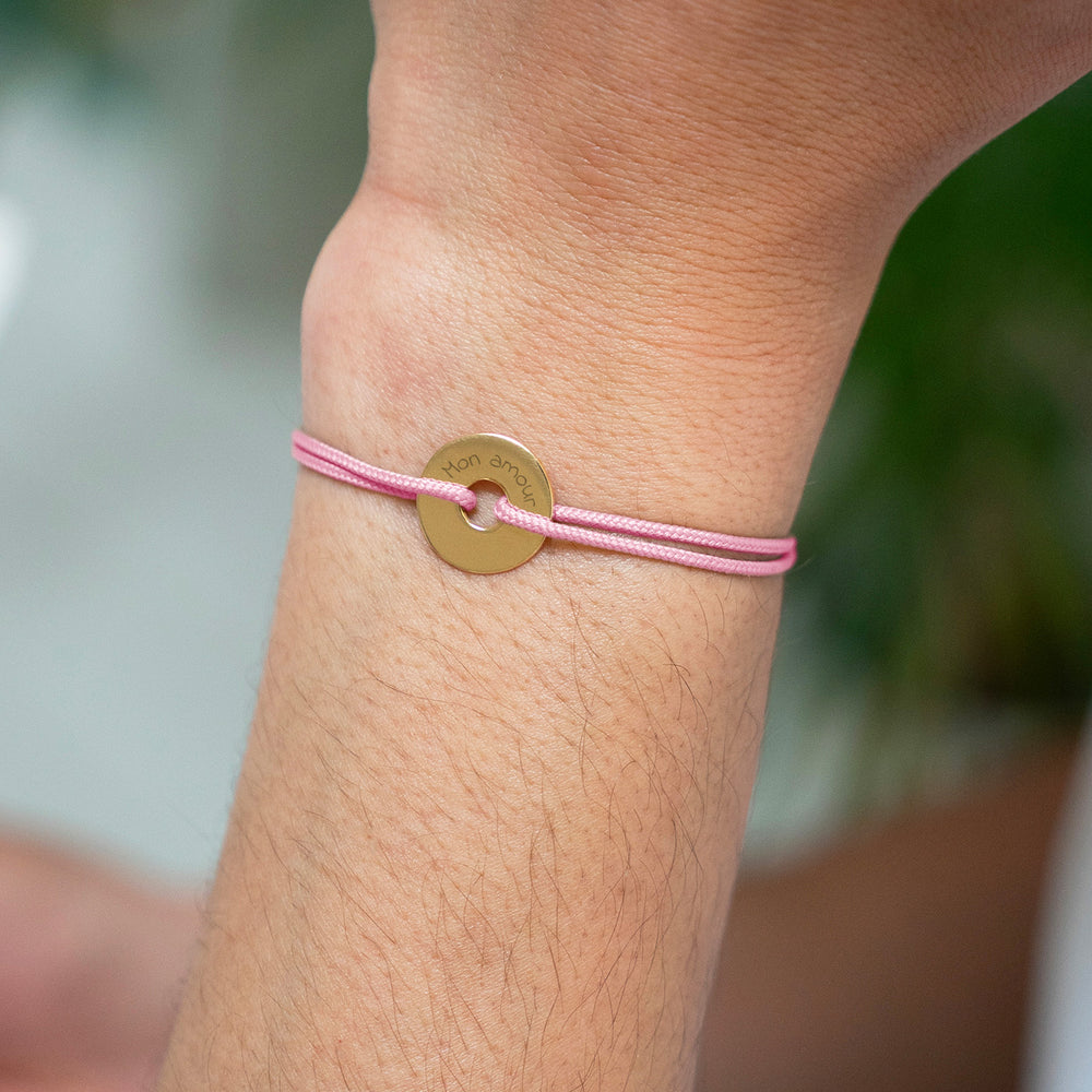 Le bracelet en plaqué or adopte une forme cible personnalisée en 15mm, accompagnée d'un cordon rose.