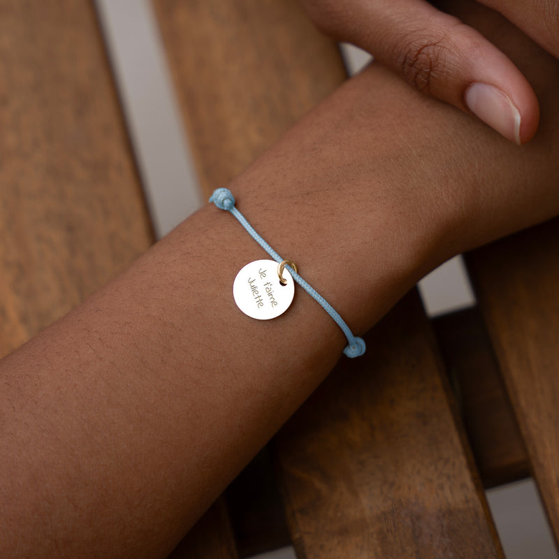 Complétez votre look avec ce bracelet en cordon bleu pastel, rehaussé d'une médaille plaquée or de 15mm, pour une allure raffinée et moderne.