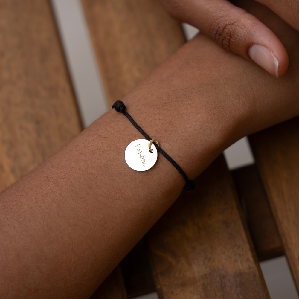 Un bracelet en plaqué or avec une médaille de 15mm, monté sur un cordon noir élégant.